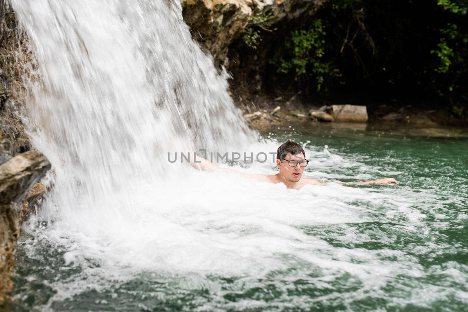 Man swimming in the mountain river with a waterfall by Desperada