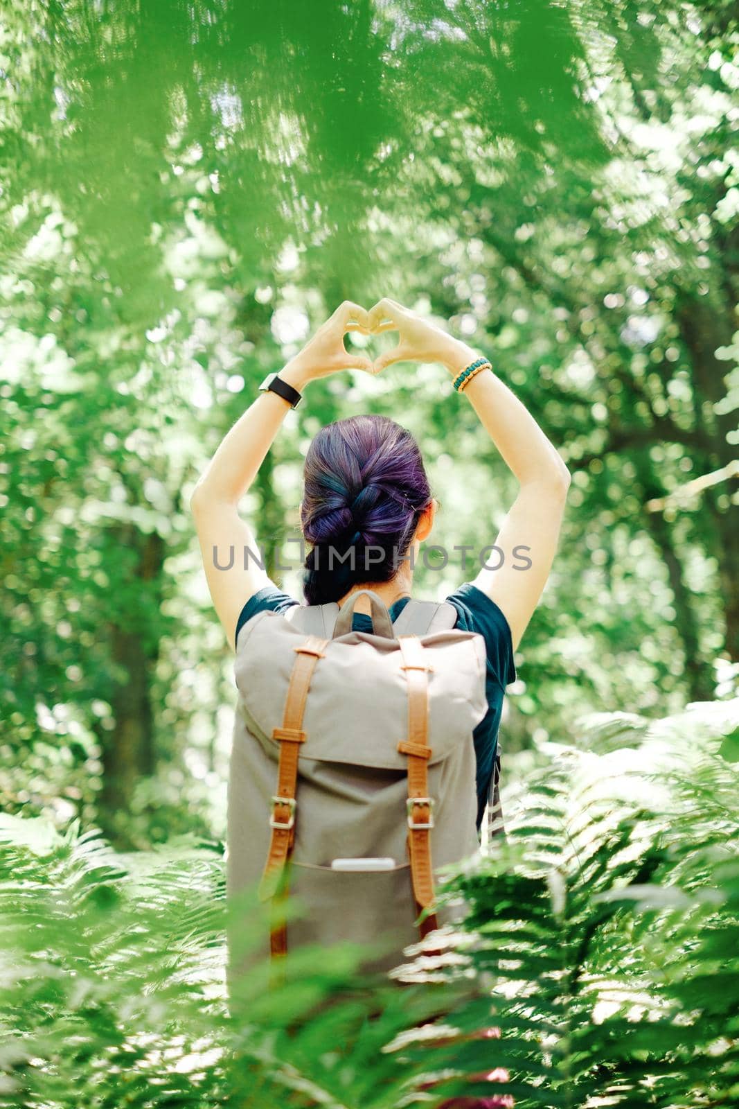 Backpacker young woman standing in summer forest and making heart shape with her hands.