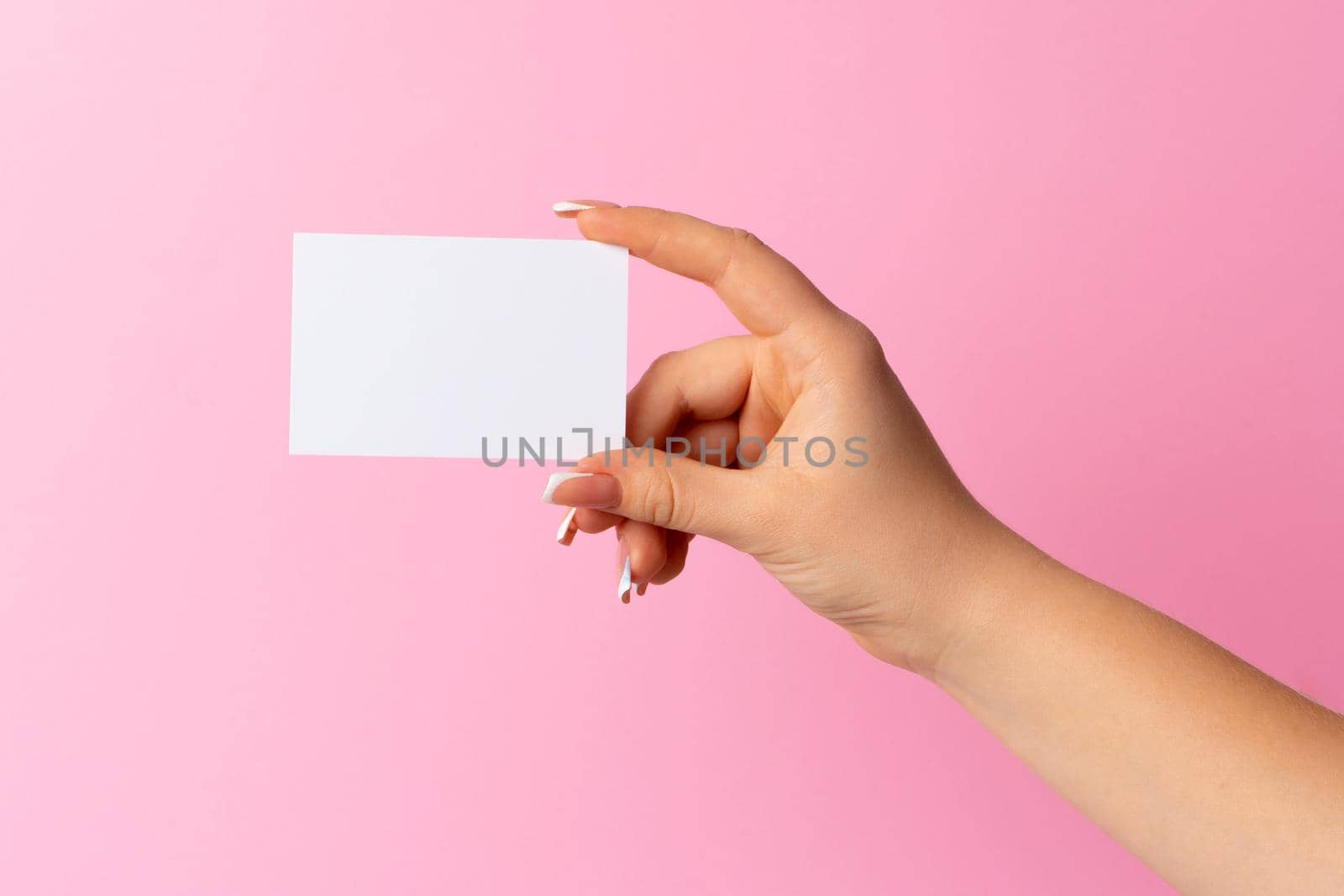 Woman hand showing blank business card on pink background. Close up.