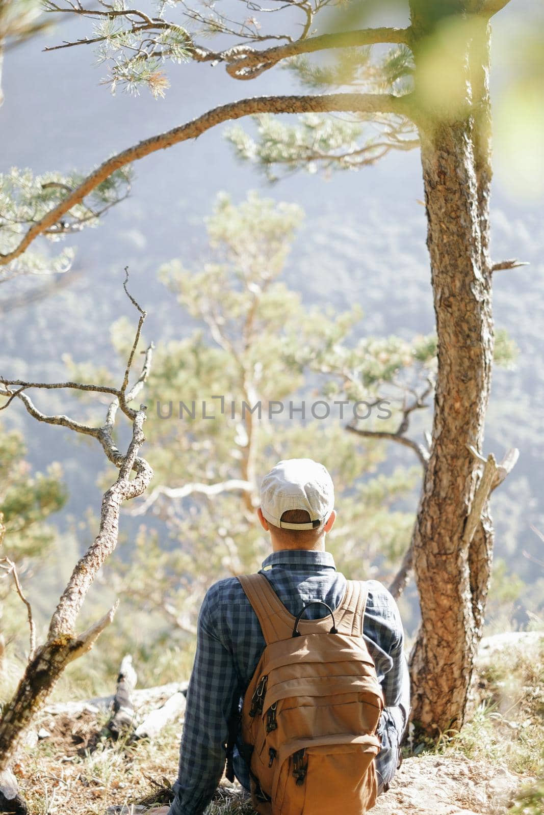 Backpacker young man resting near the tree and enjoying view of nature.