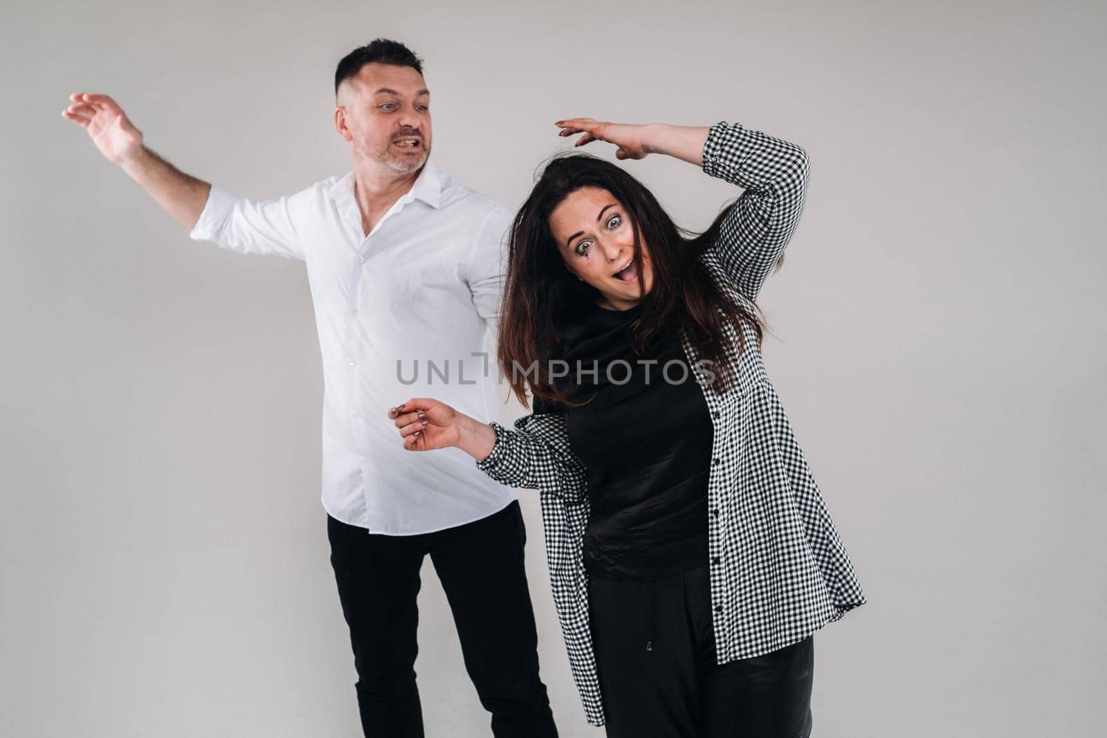 A man swings his fist at a battered woman standing on a gray background. Domestic violence.