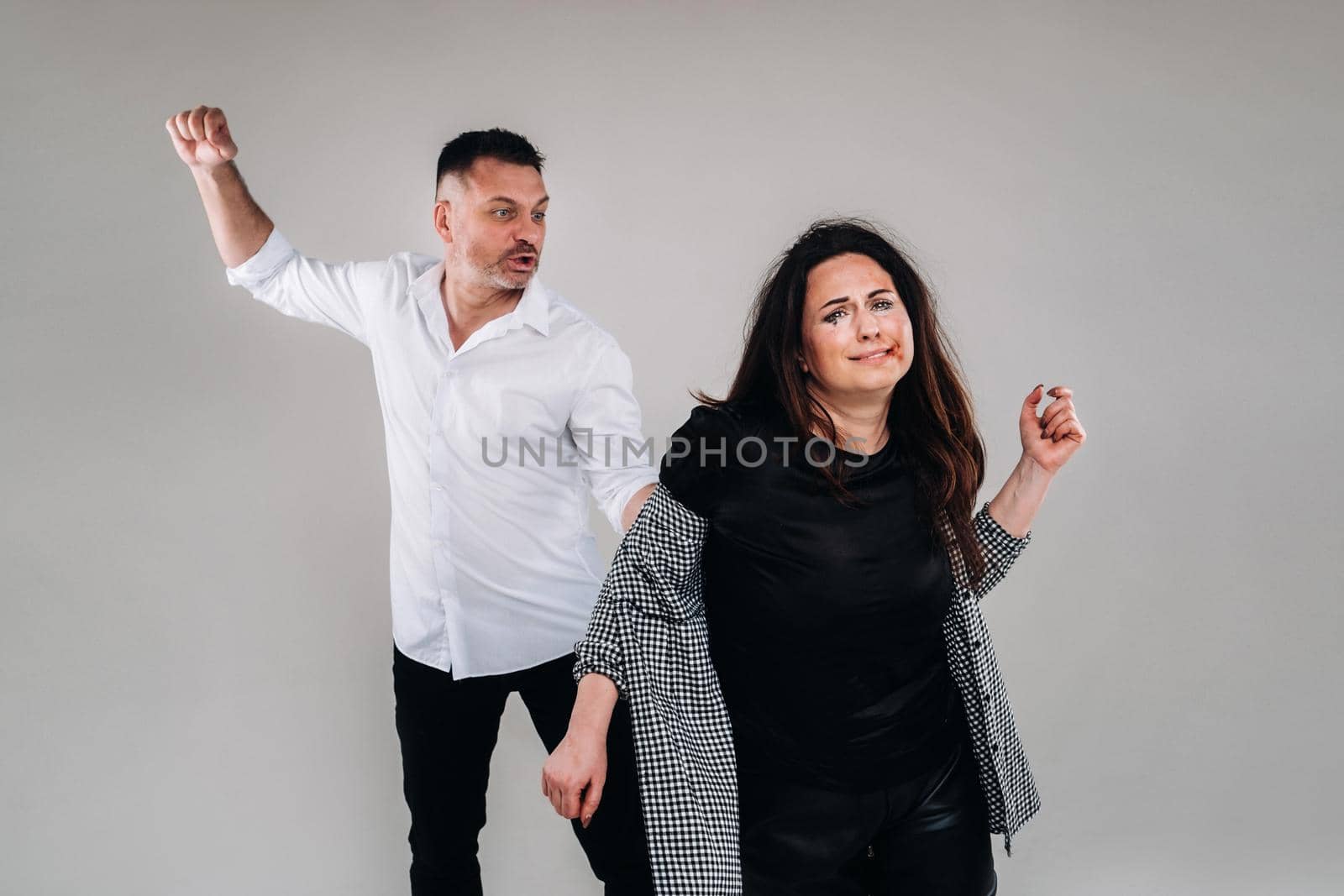 A man swings his fist at a battered woman standing on a gray background. Domestic violence by Lobachad