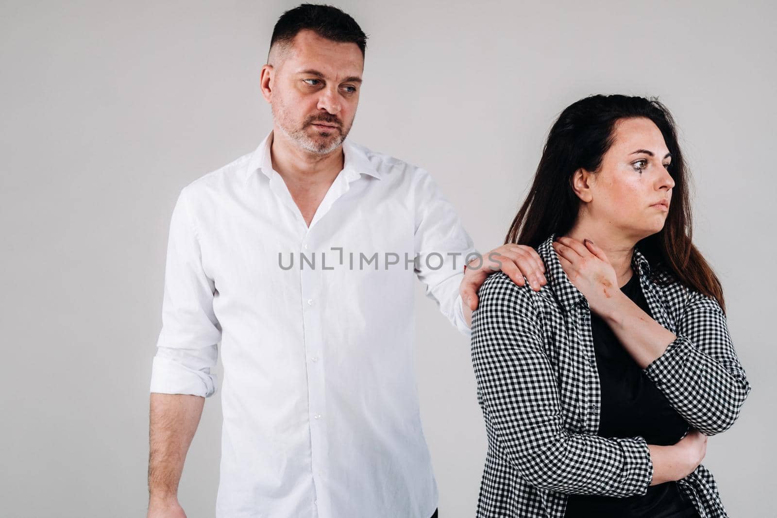 A woman beaten by her husband standing behind her and looking at her aggressively. Domestic violence.