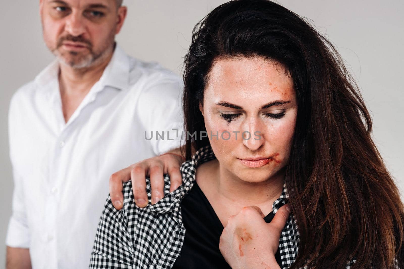 A woman beaten by her husband standing behind her and looking at her aggressively. Domestic violence.