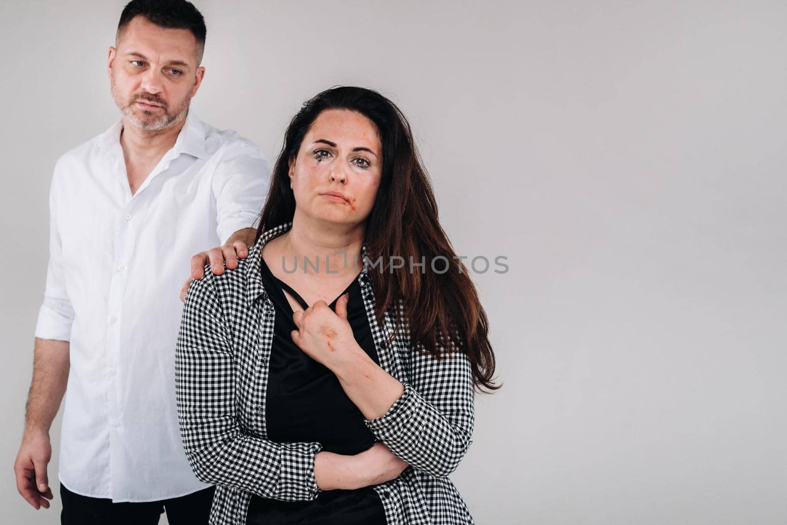 the male rapist put his hand on the shoulder of the beaten woman on a gray background. Domestic violence by Lobachad