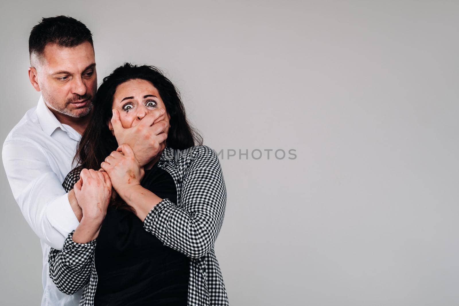An aggressive man covers the mouth of a beaten woman so that she cannot scream. Domestic violence.