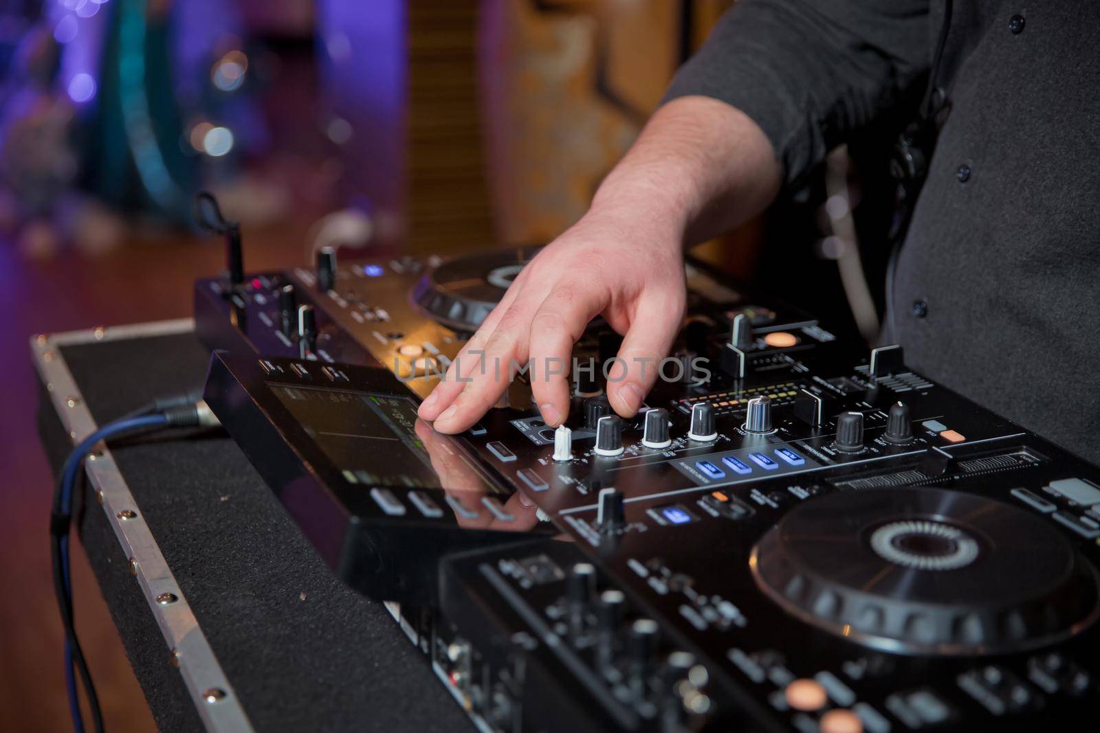 Men's hands press the buttons on the DJ remote, it makes music . DJ's hands at the music mixer at a party - playing some fine songs for the guests color toned image by Adil_Celebiyev_Stok_Photo
