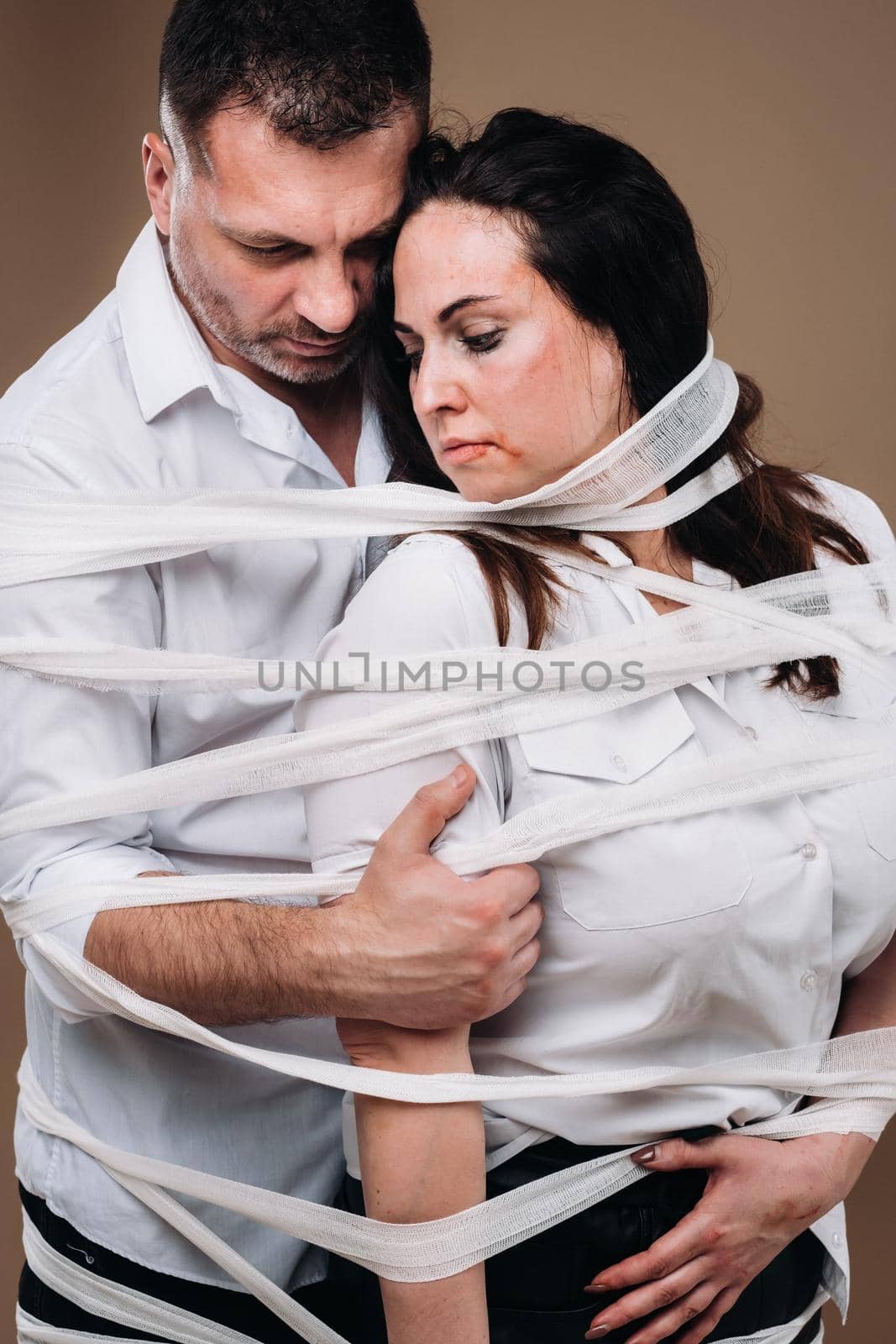 An aggressive man embraces a battered woman and is wrapped in bandages together. Domestic violence by Lobachad