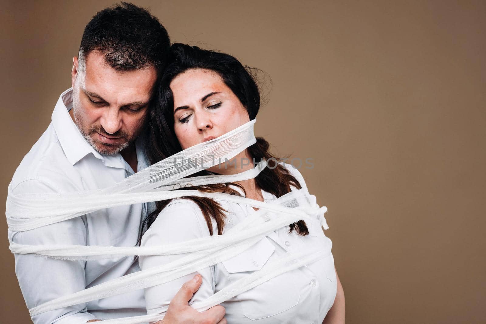 An aggressive man embraces a battered woman and is wrapped in bandages together. Domestic violence by Lobachad