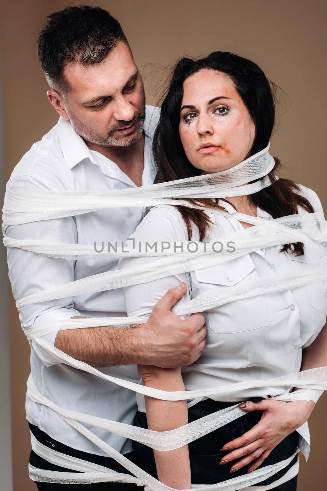 An aggressive man embraces a battered woman and is wrapped in bandages together. Domestic violence by Lobachad