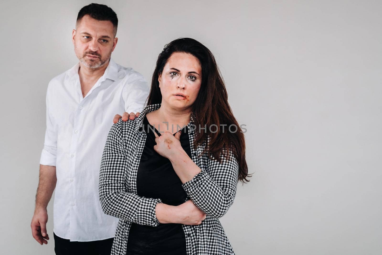 A woman beaten by her husband standing behind her and looking at her aggressively. Domestic violence.