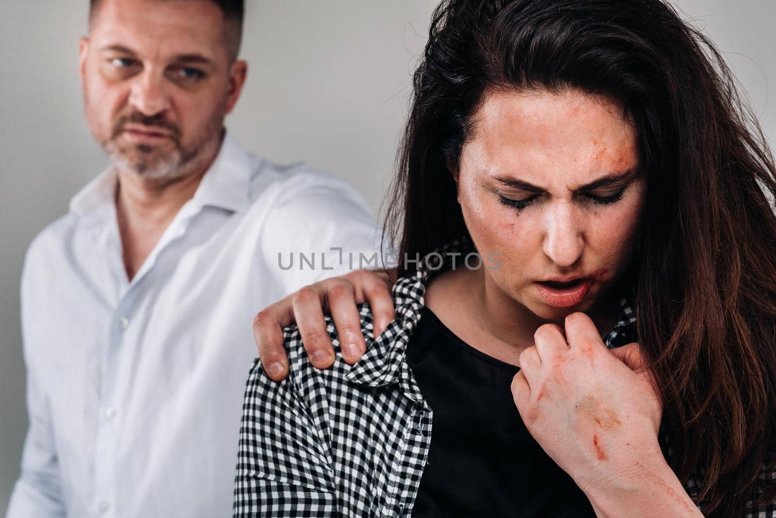A woman beaten by her husband standing behind her and looking at her aggressively. Domestic violence by Lobachad