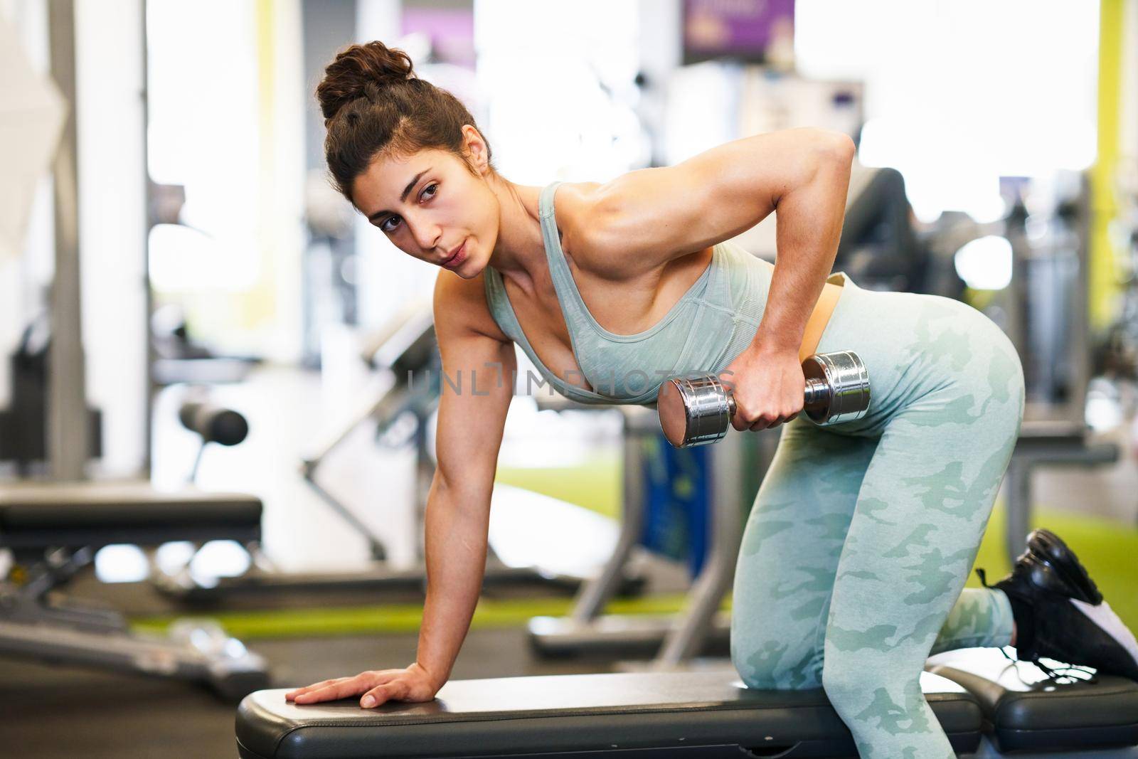 Caucasian strong woman lifting some weights and working on her triceps and biceps in a gym with dumbbells.