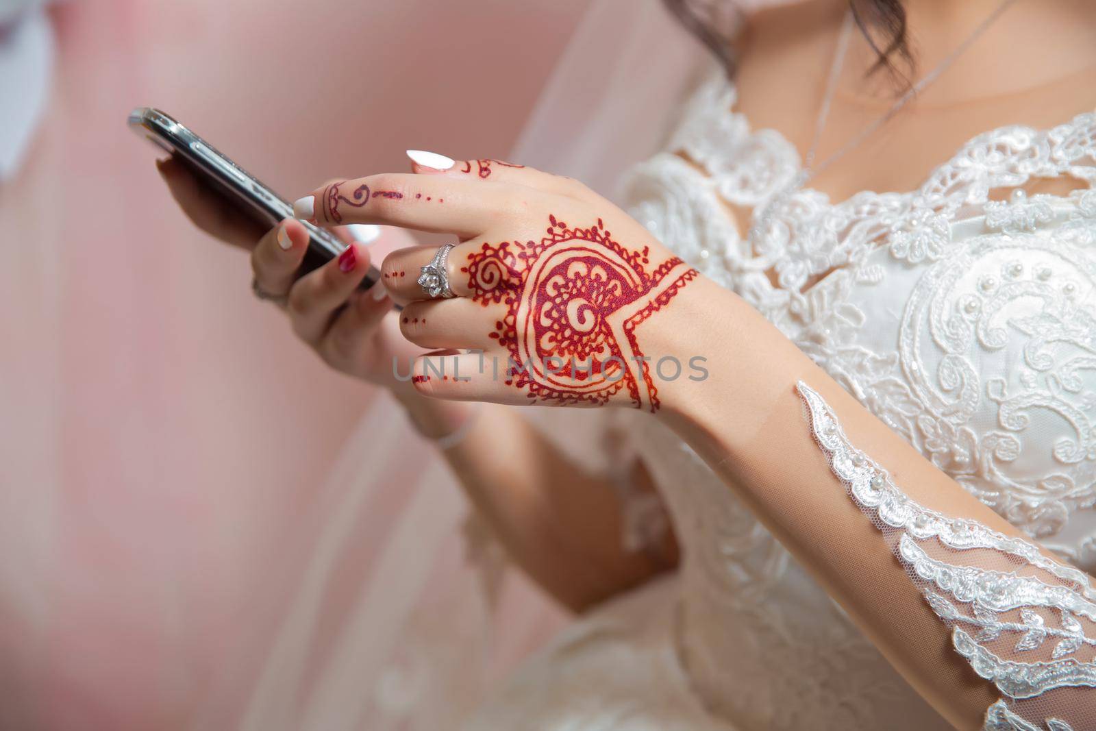 The bride holds a phone . The bride has a ring in her hands . The bride has a henna.