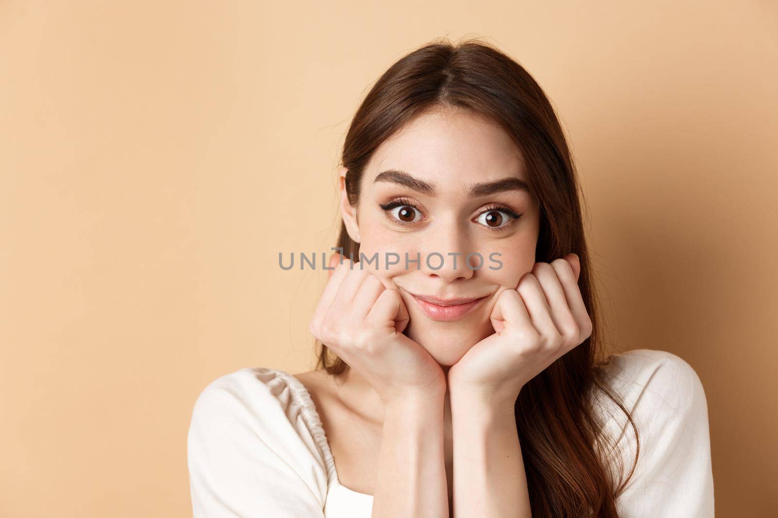 Portrait of intrigued girl listening with interest and excitement, hear interesting story, smiling amused, standing on beige background.