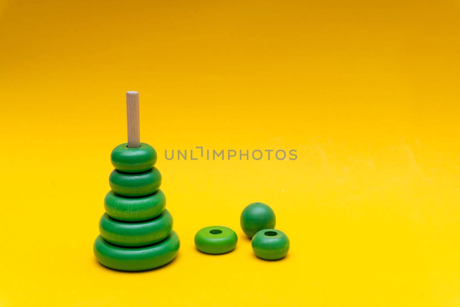 Pyramid build from green children wooden toy rings at yellow background, toy for baby and toddlers. Child development concept.