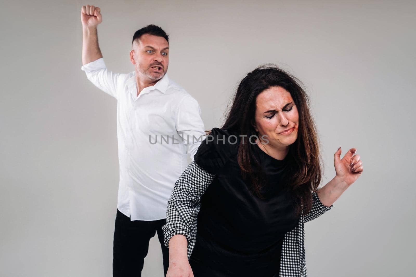 A man swings his fist at a battered woman standing on a gray background. Domestic violence.