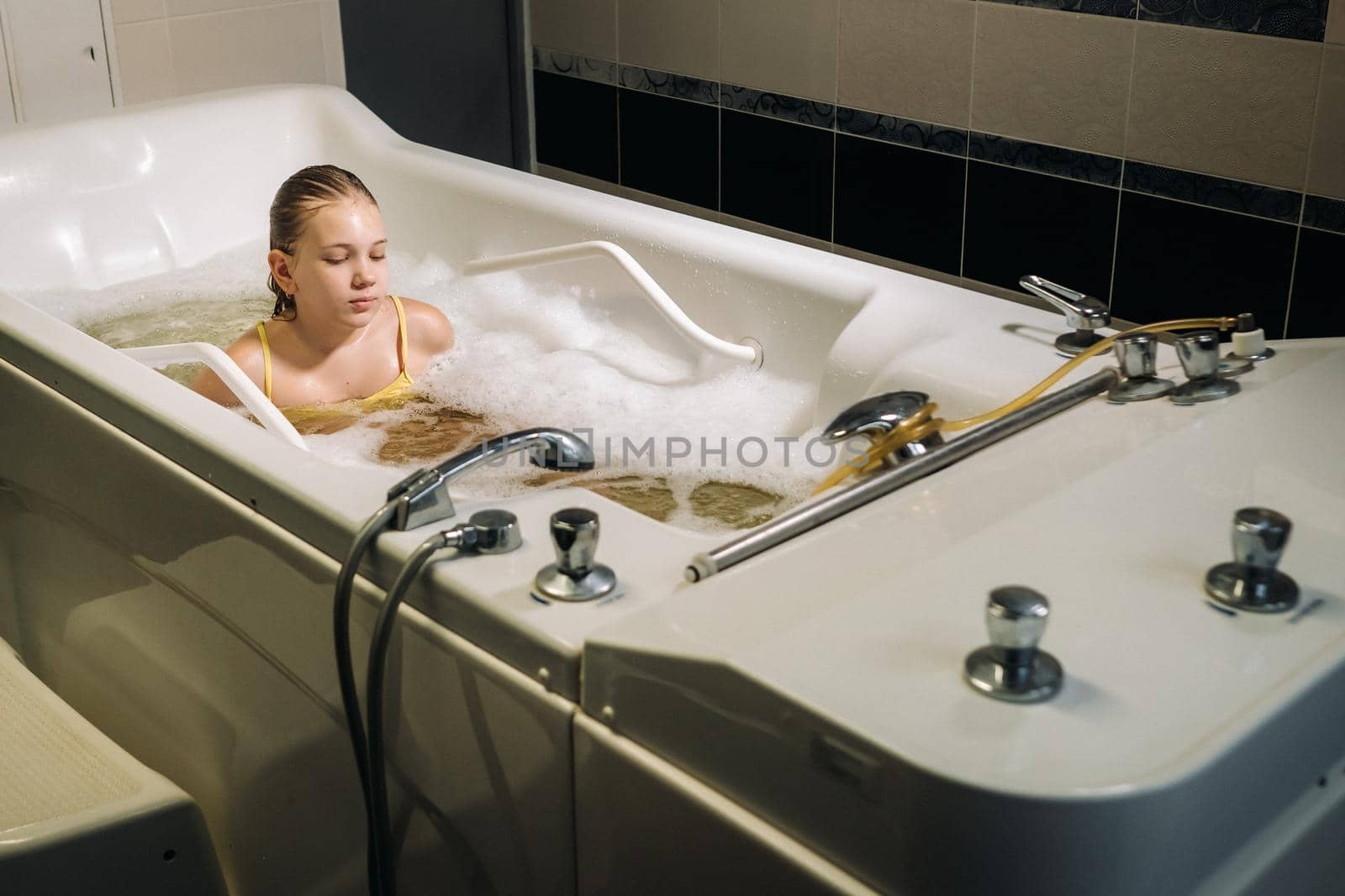 a little girl takes the procedure in a mineral bath. The patient receives water treatments with a mineral pearl bath by Lobachad