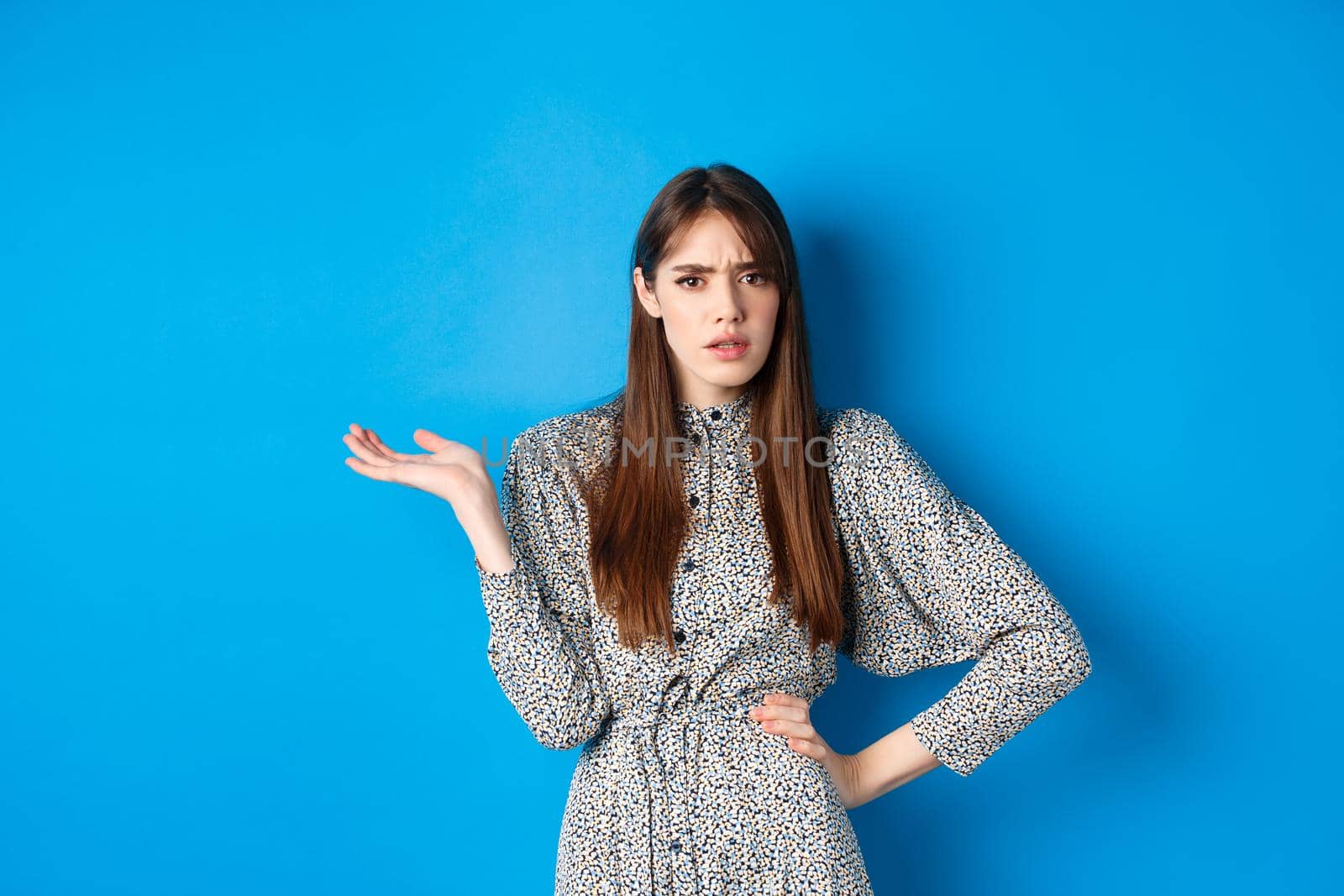 Confused and annoyed girl arguing, raising hand up and frowning, cant understand what big deal, standing on blue background.