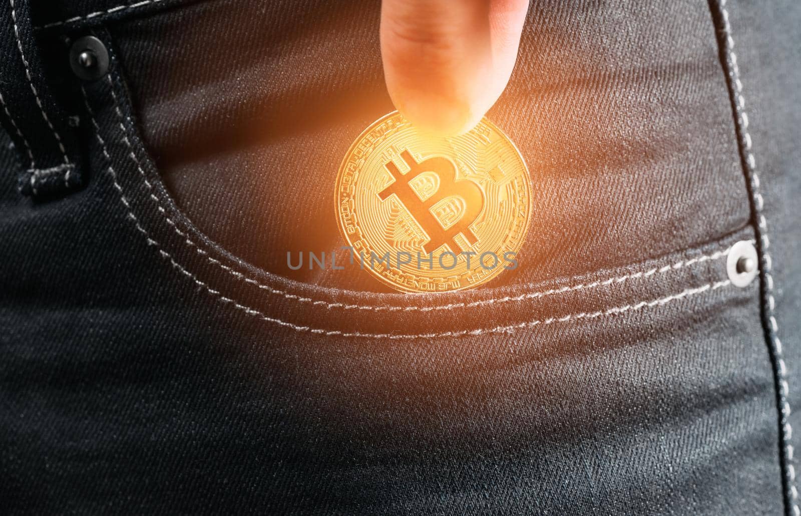 Male hand holding gold bitcoin and putting into pocket of jeans, close-up.