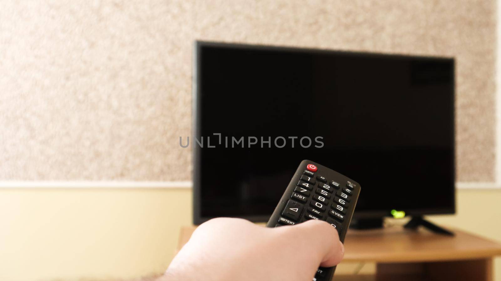Hand holding a television remote control and surfing programs on television. watch, turn on or off the TV in the living room or bedroom on the black-screen nightstand. Copy space. by Roshchyn
