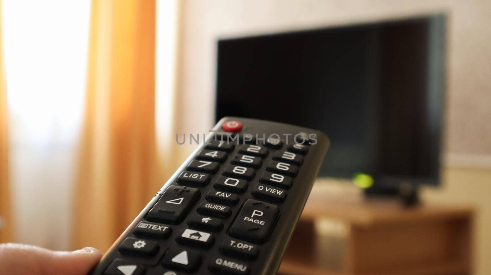 Hand holding a television remote control and surfing programs on television. watch, turn on or off the TV in the living room or bedroom on the black-screen nightstand. Copy space
