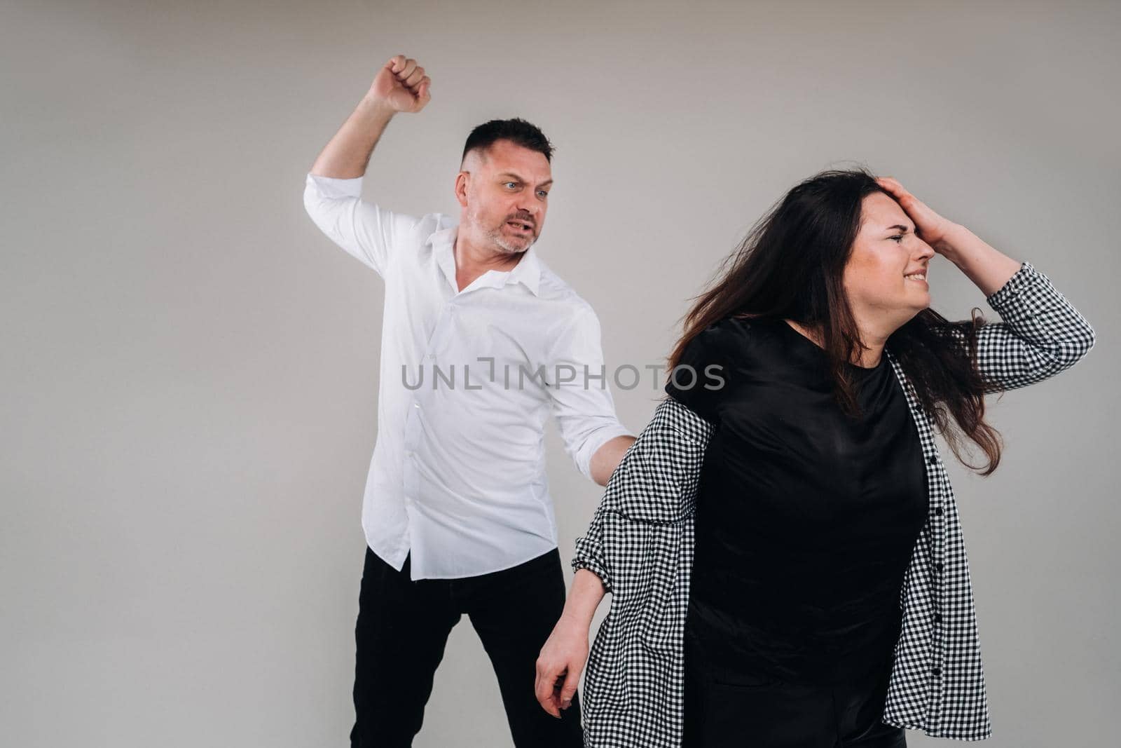 A man swings his hand at a battered woman standing on a gray background. Domestic violence by Lobachad