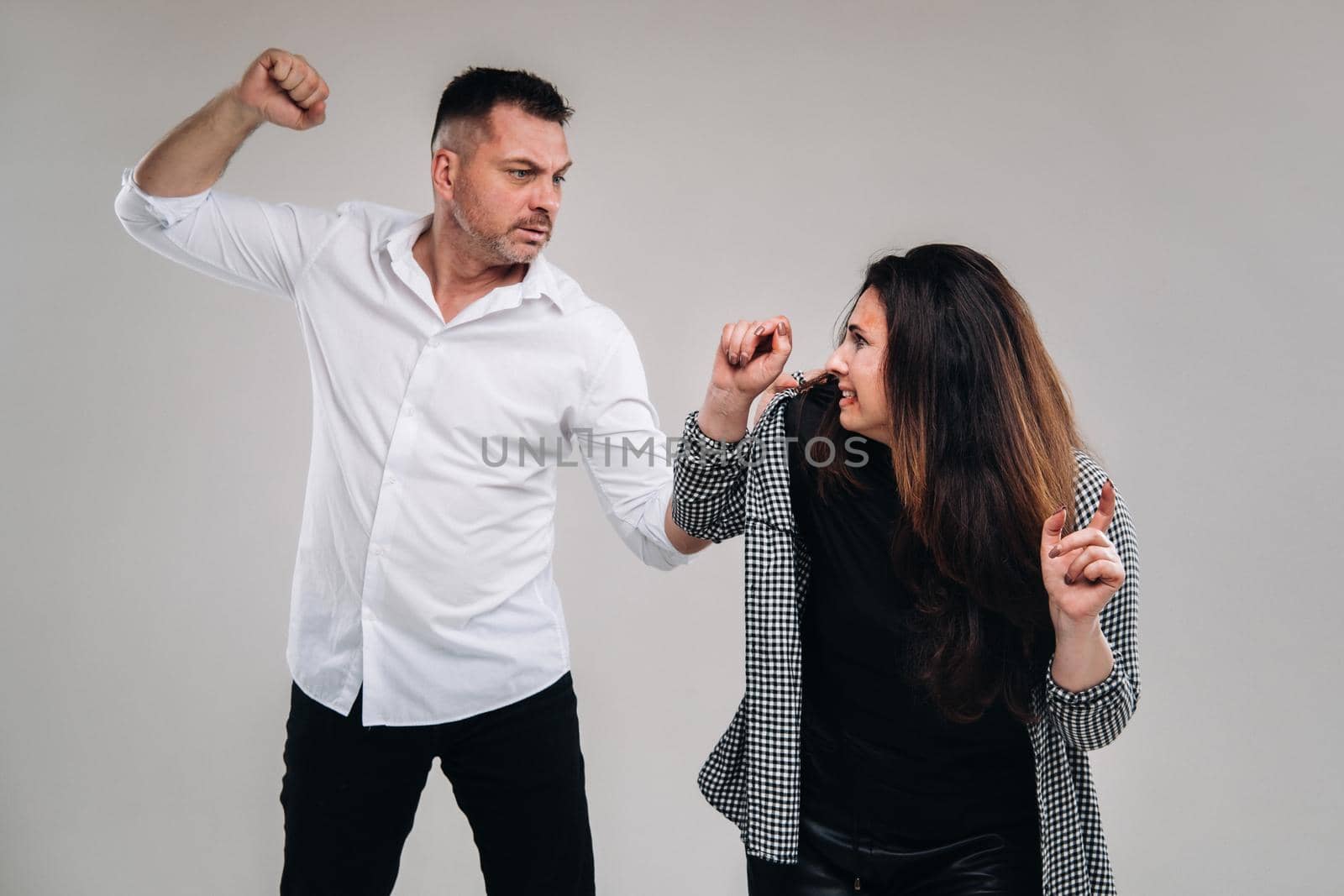 A man swings his fist at a battered woman standing on a gray background. Domestic violence.