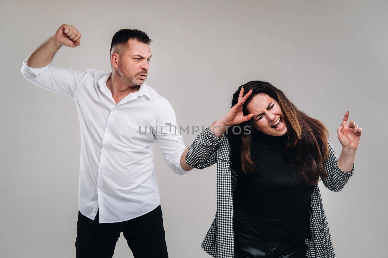 A man swings his fist at a battered woman standing on a gray background. Domestic violence.