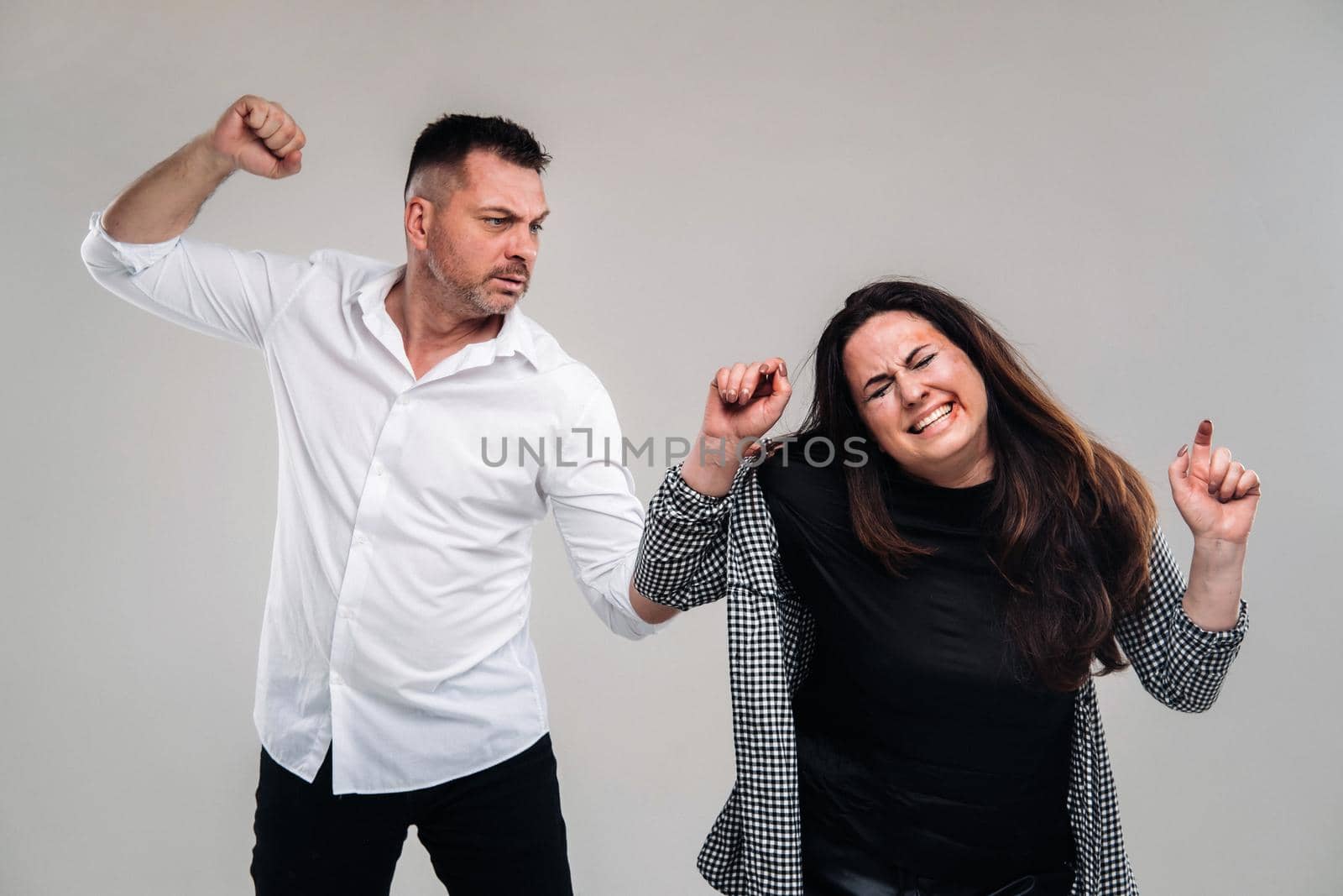 A man swings his fist at a battered woman standing on a gray background. Domestic violence.