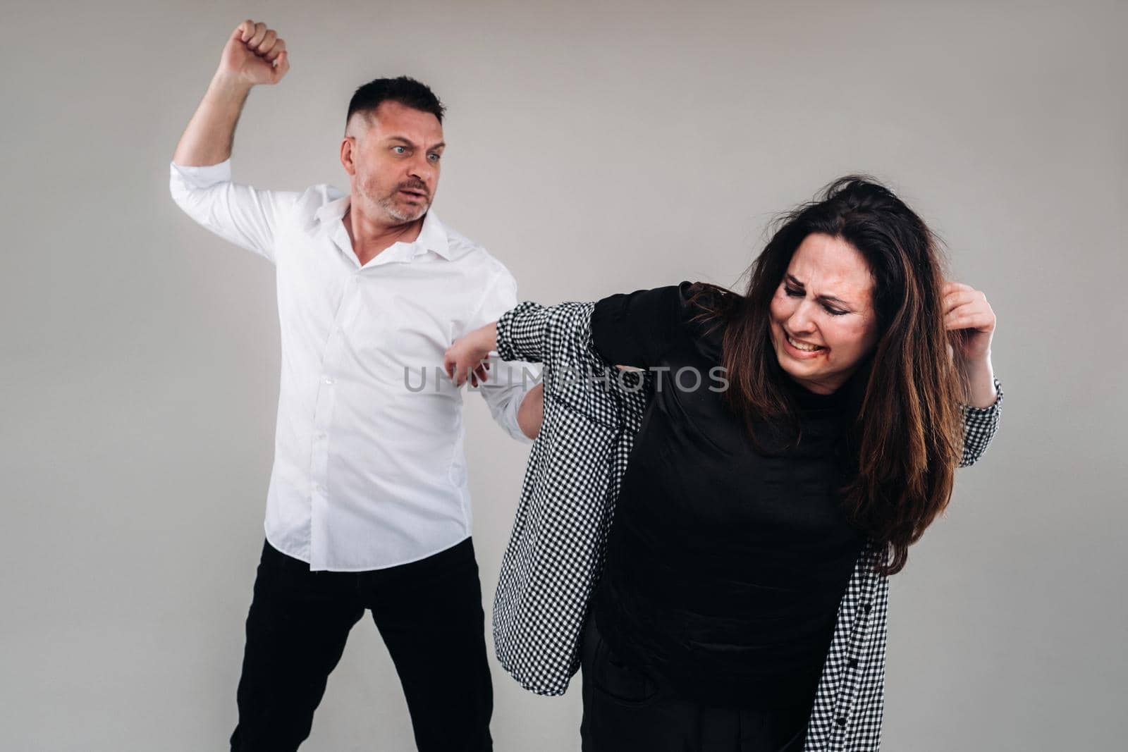 A man swings his fist at a battered woman standing on a gray background. Domestic violence by Lobachad
