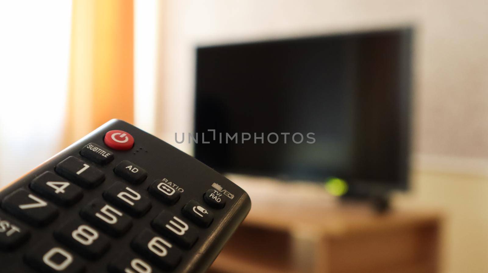 Hand holding a television remote control and surfing programs on television. watch, turn on or off the TV in the living room or bedroom on the black-screen nightstand. Copy space. by Roshchyn