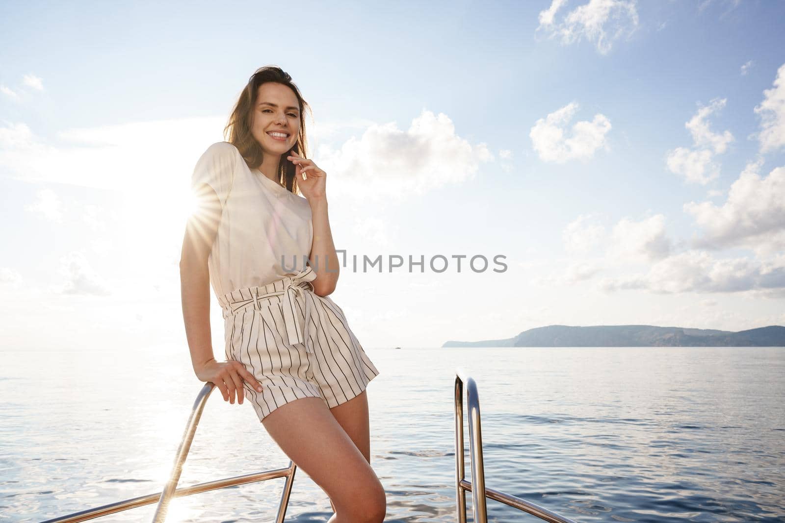 Young brunette woman standing on the nose of the yacht at a sunny summer day, close up