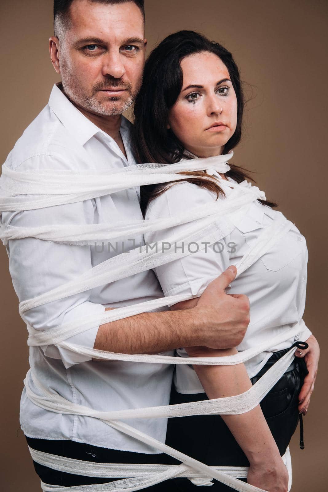An aggressive man embraces a battered woman and is wrapped in bandages together. Domestic violence.