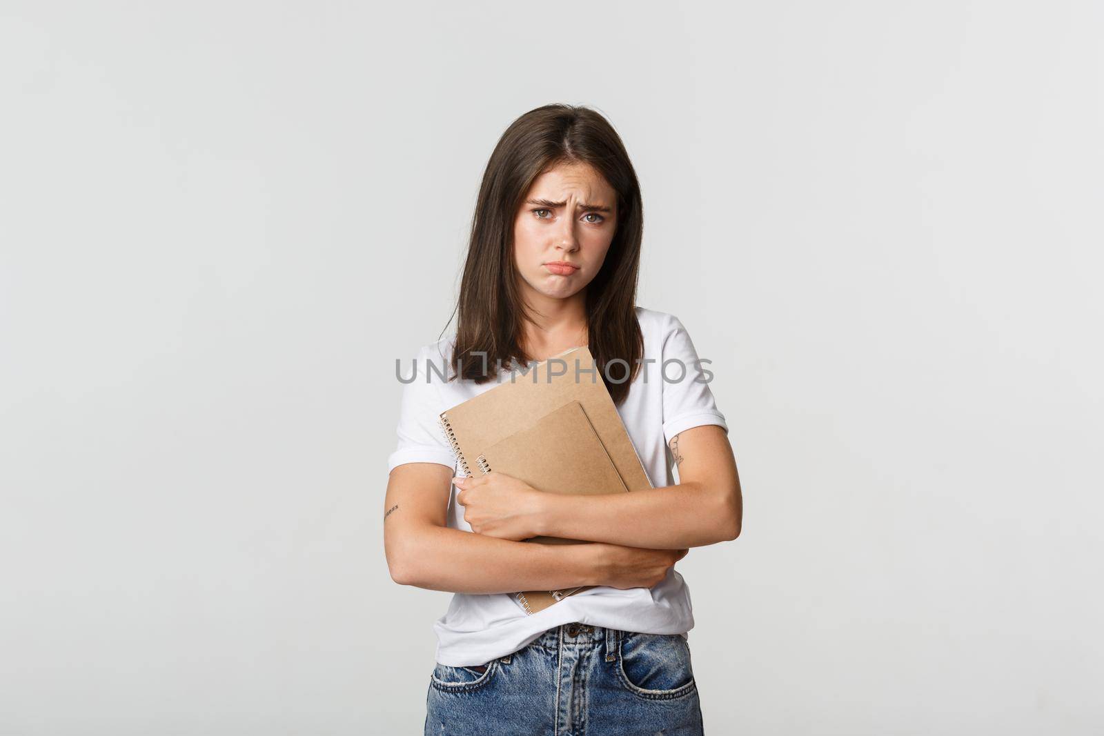 Portrait of gloomy and miserable cute girl with notebooks, frowning and looking sad at camera.