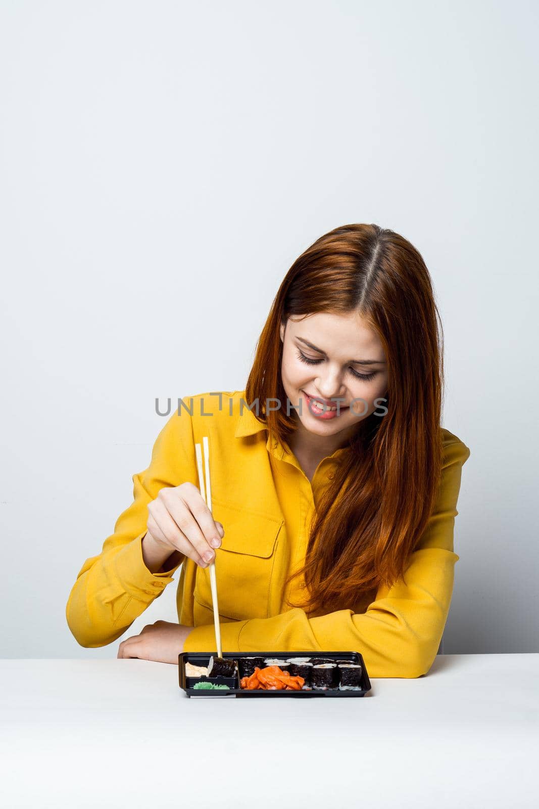 a woman in a yellow shirt sits at a table and eats sushi. High quality photo