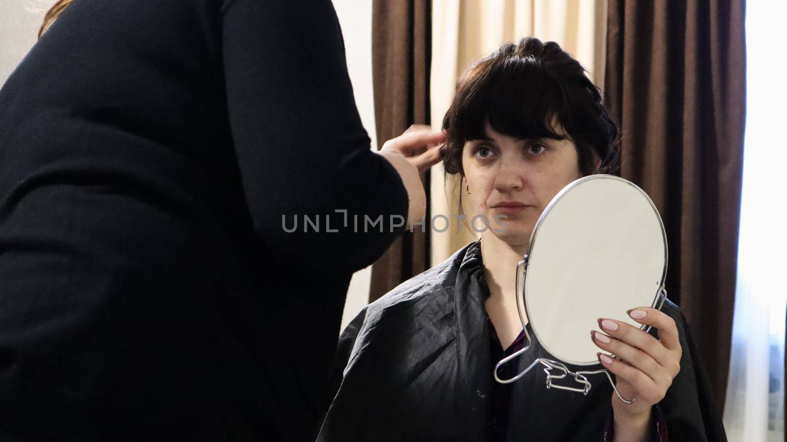 Close up of master hairdresser doing curly hairstyle and makeup for beautiful woman with dark hair at home. Wedding hairstyle for the bride