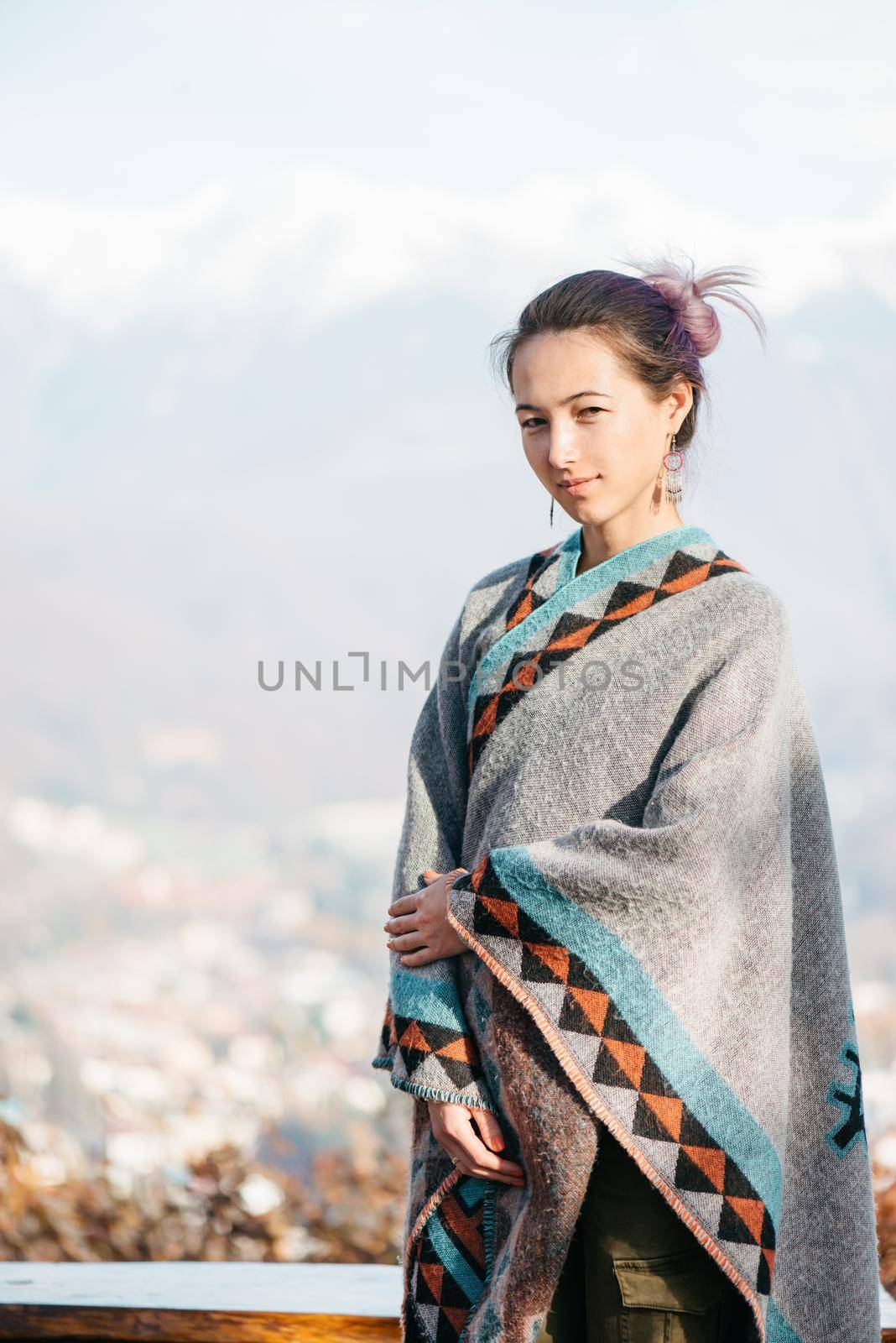 Beautiful young woman standing on background of snowy mountains, looking at camera.