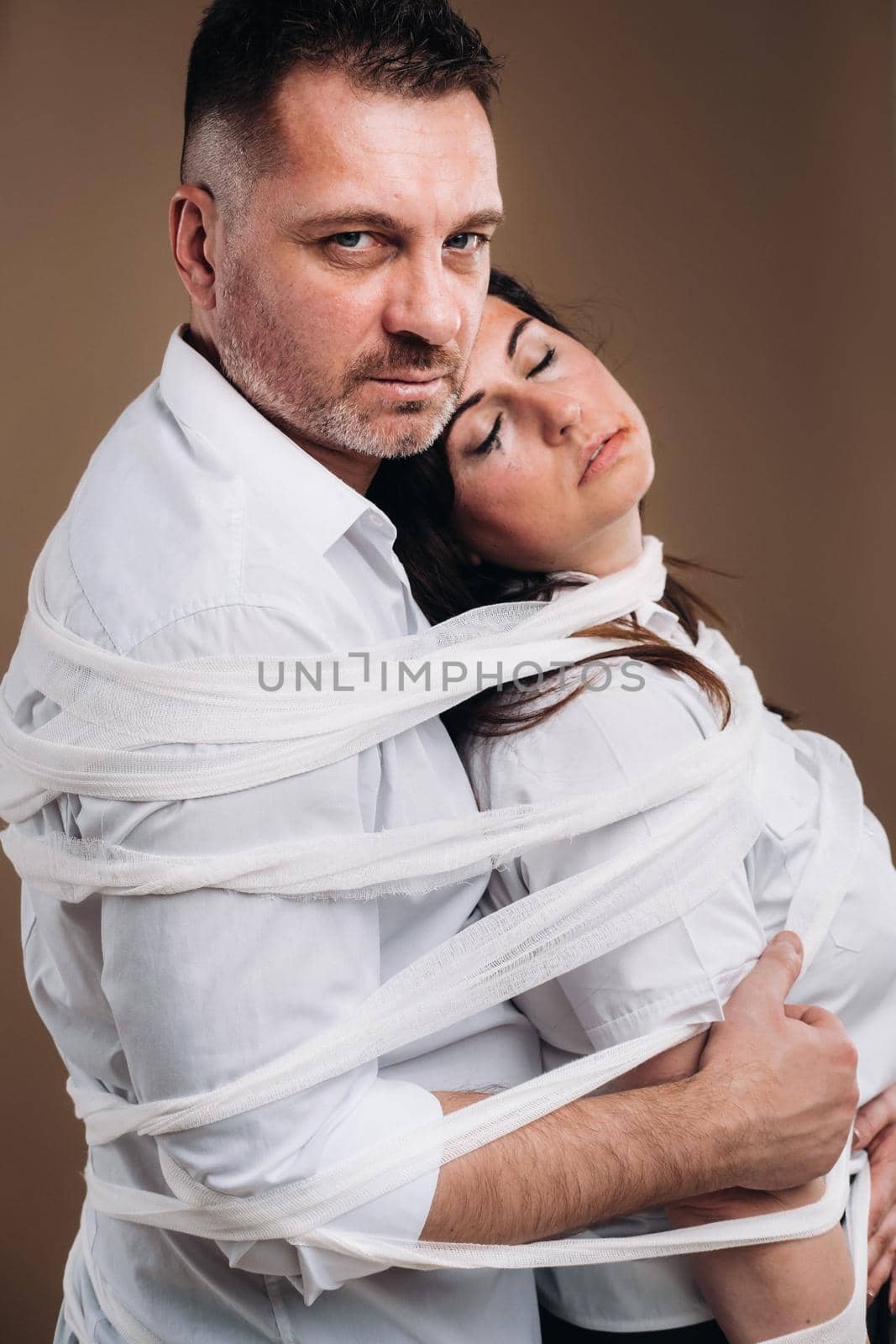 An aggressive man embraces a battered woman and is wrapped in bandages together. Domestic violence.