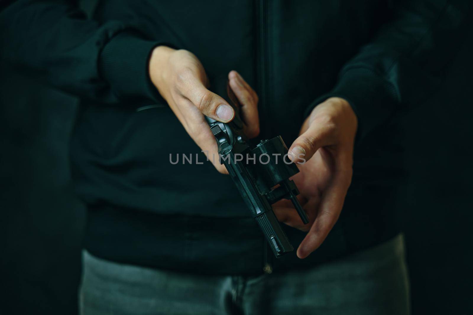 Reloading gun close-up. Men's hands check for bullets in revolver barrel. Guy in jeans and black hoodie prepares pistol for shots. Firearm for defense or attack.