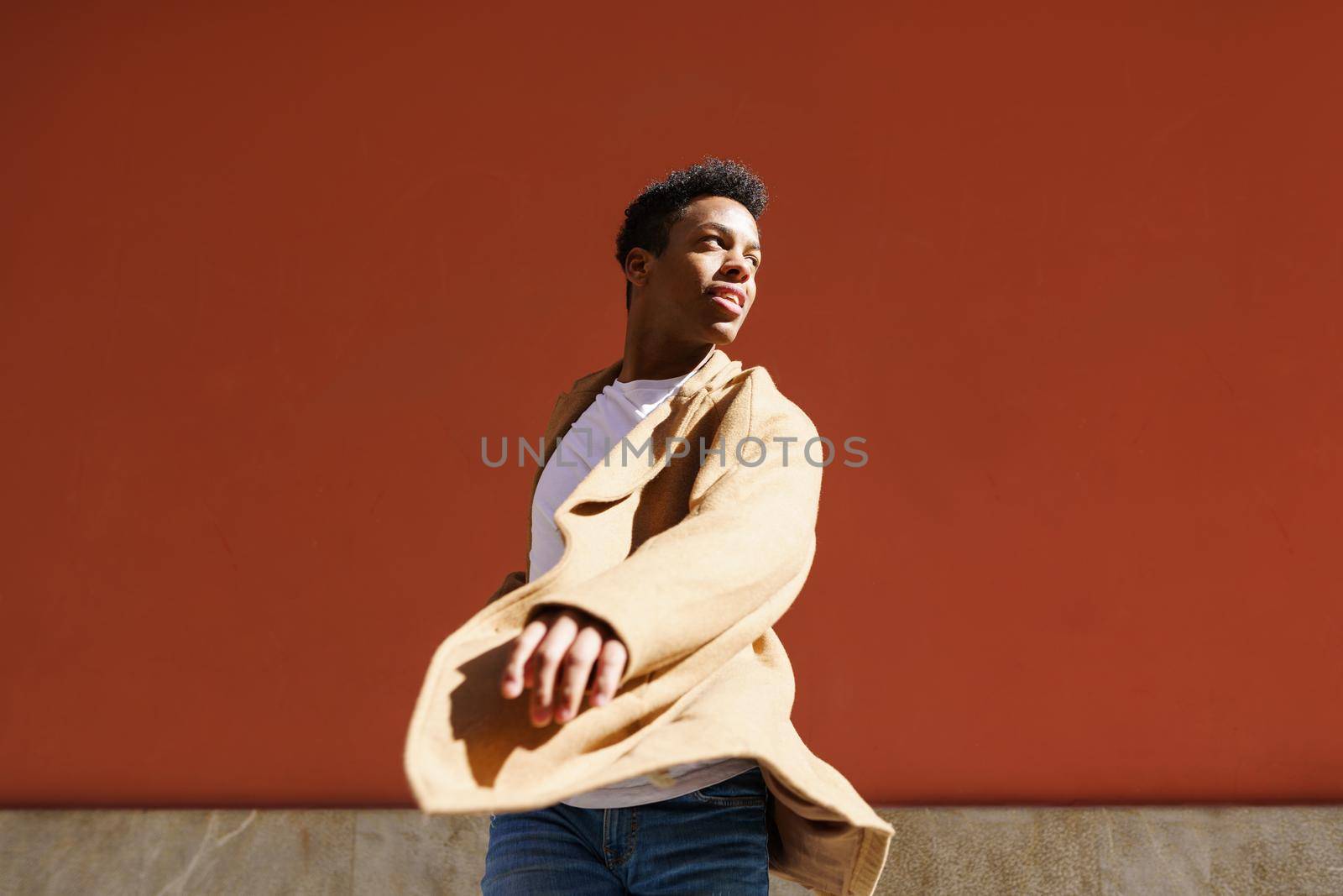 Young Cuban man dancing on red urban wall. Happy young black guy outdoors.