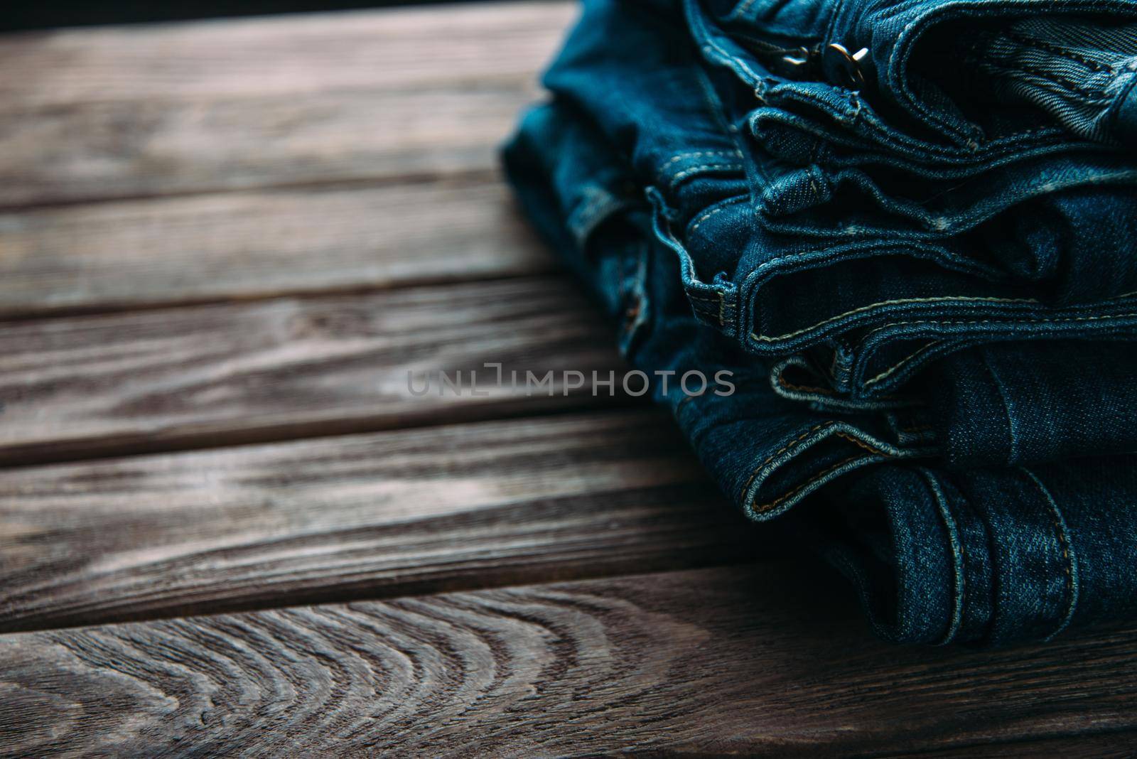 Stack of blue jeans denim pants on a wooden table.