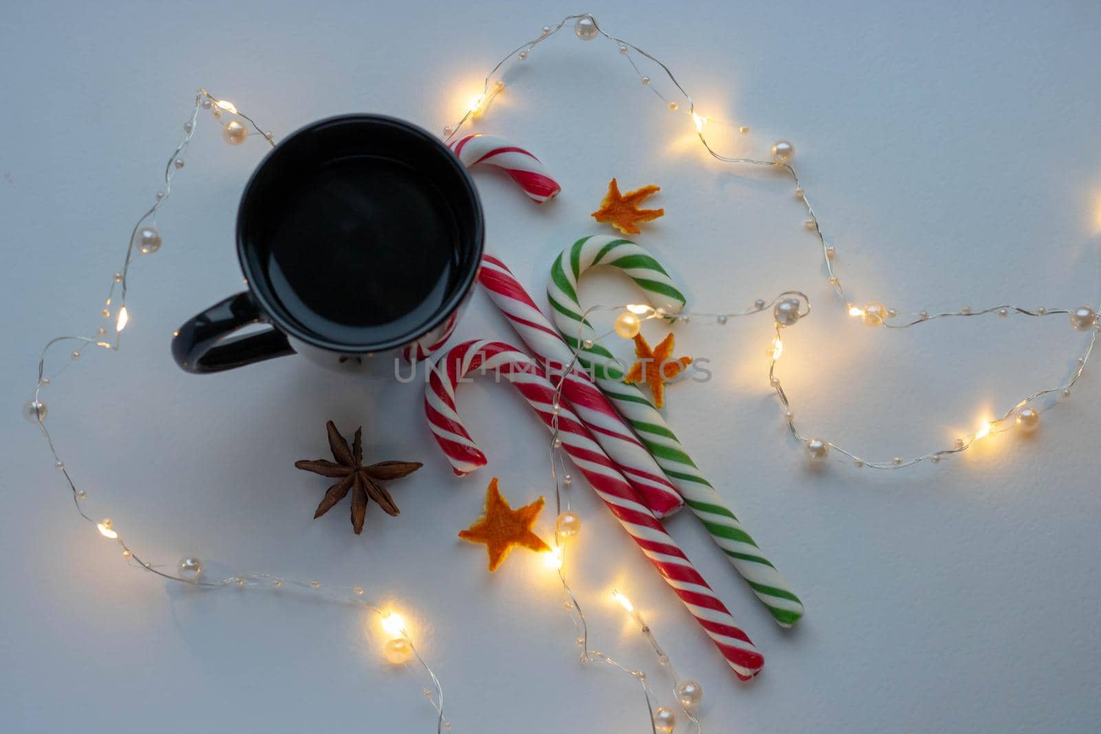 New year's concept of Christmas and winter. A black Cup of hot coffee, a candy cane, and a garland on a white background. The view from the top. Holiday Breakfast. by lapushka62
