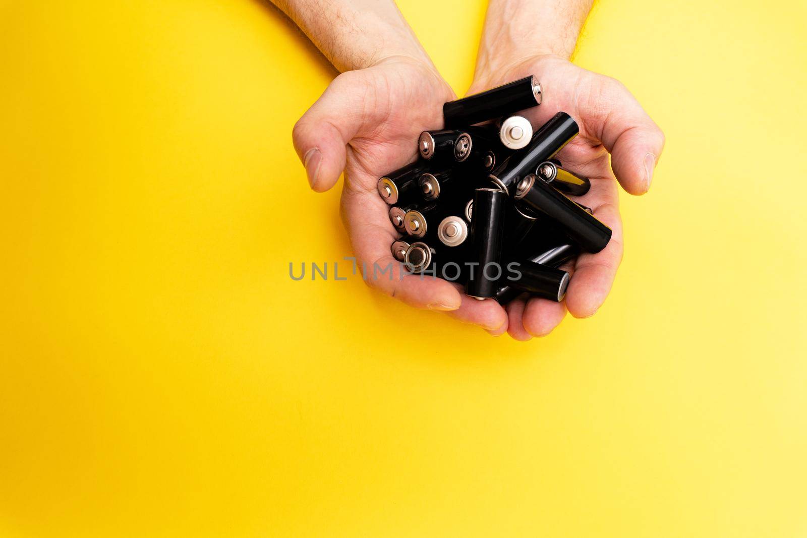 A lot of black aa batteries in male hands on yellow background, view from the top, minimal concept, copy space.