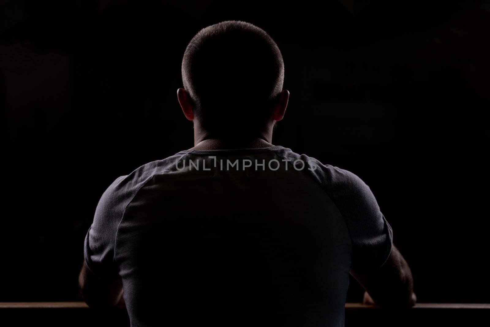 Silhouette of a young guy who sits. Close-up view from behind. Backlight.