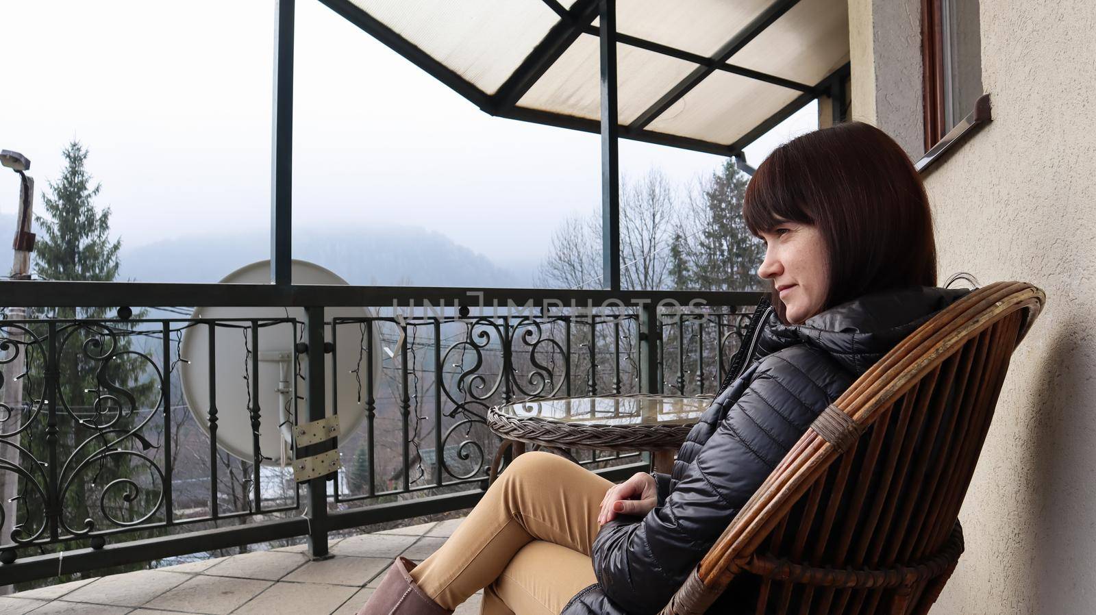 Beautiful happy woman enjoying the wonderful view of the mountain landscape in the morning fog from the balcony of her hotel room. Autumn and winter travel concept by Roshchyn