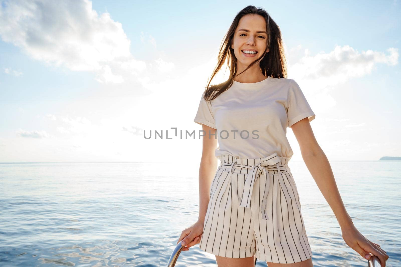 Young brunette woman standing on the nose of the yacht at a sunny summer day, close up