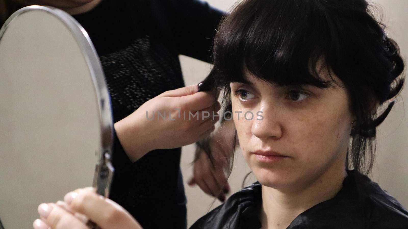 Close up of master hairdresser doing curly hairstyle and makeup for beautiful woman with dark hair at home. Wedding hairstyle for the bride