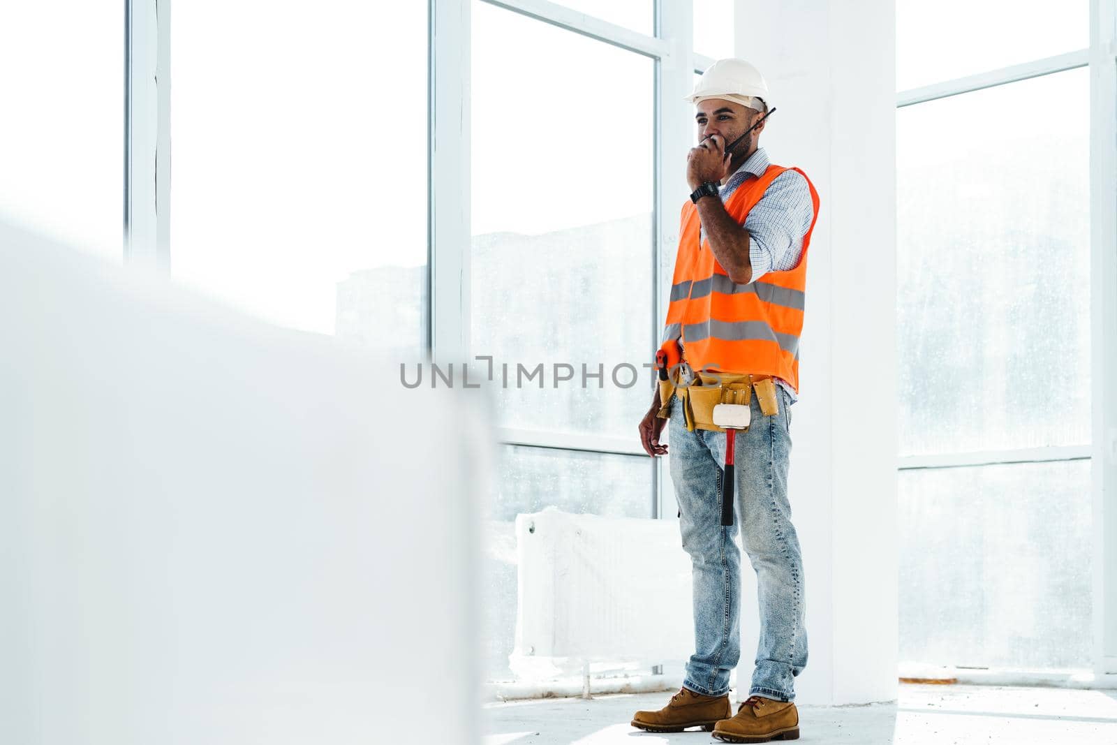 Young construction worker in uniform using walkie talkie on site, close up portrait