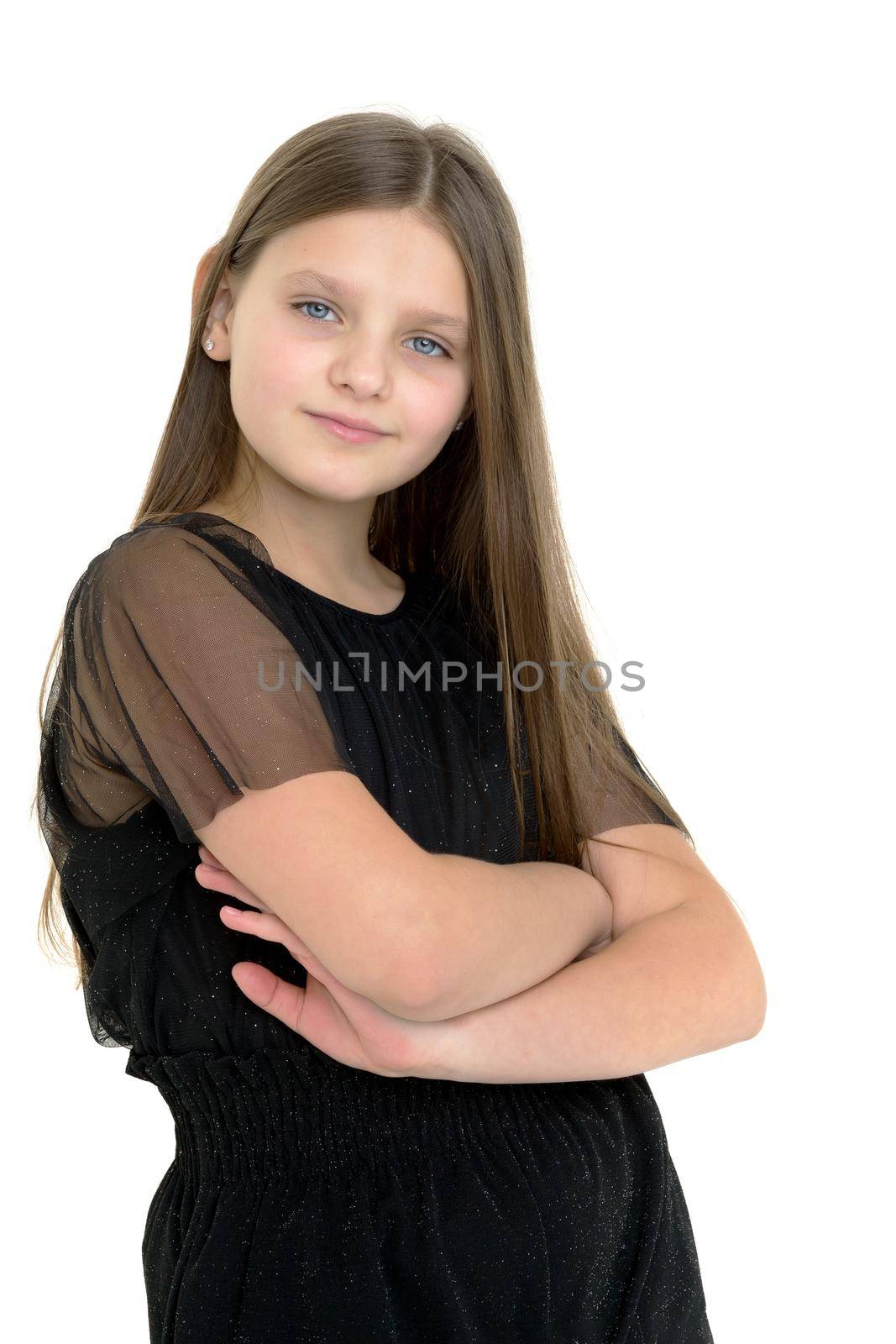 Cute girl posing in black overalls. Beautiful long-haired girl dressed in casual summer clothes, standing with folded hands on her chest on a white background, looking attentively at the camera